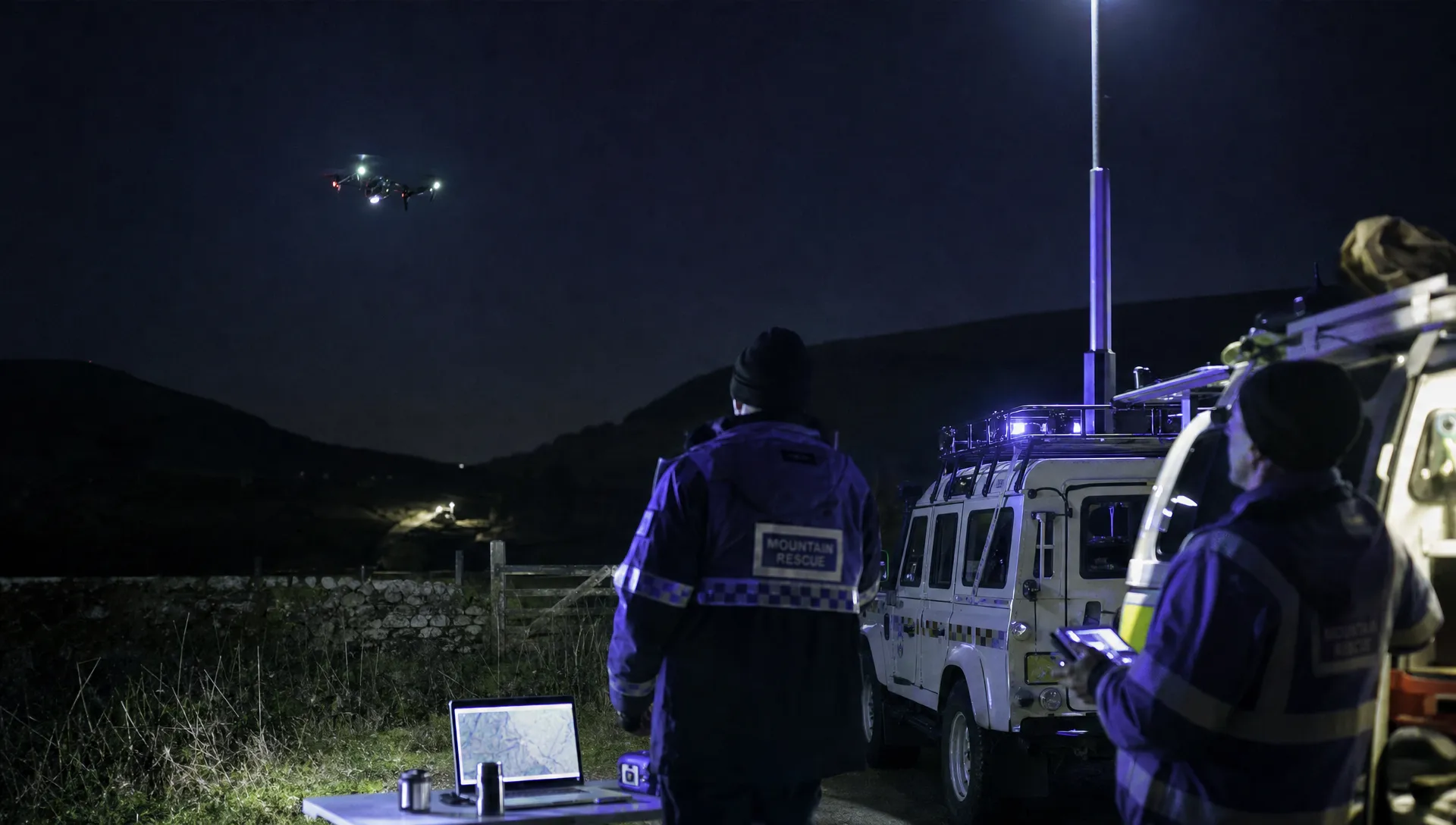 A rural night search shows a drone flying away from responders beside vehicles at the staging area.