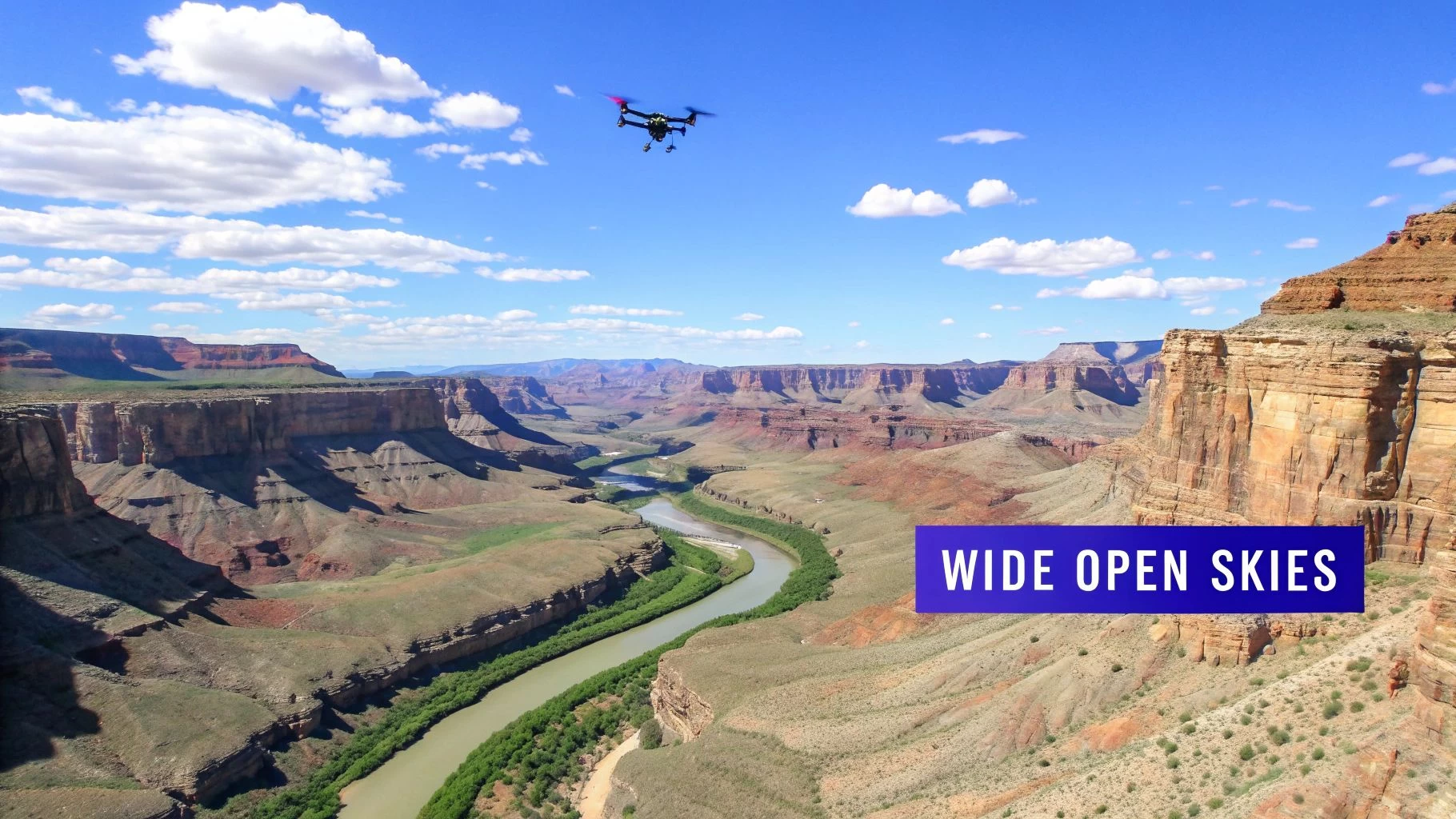 A drone flies over the vast Grand Canyon with a river, under a wide open blue sky.